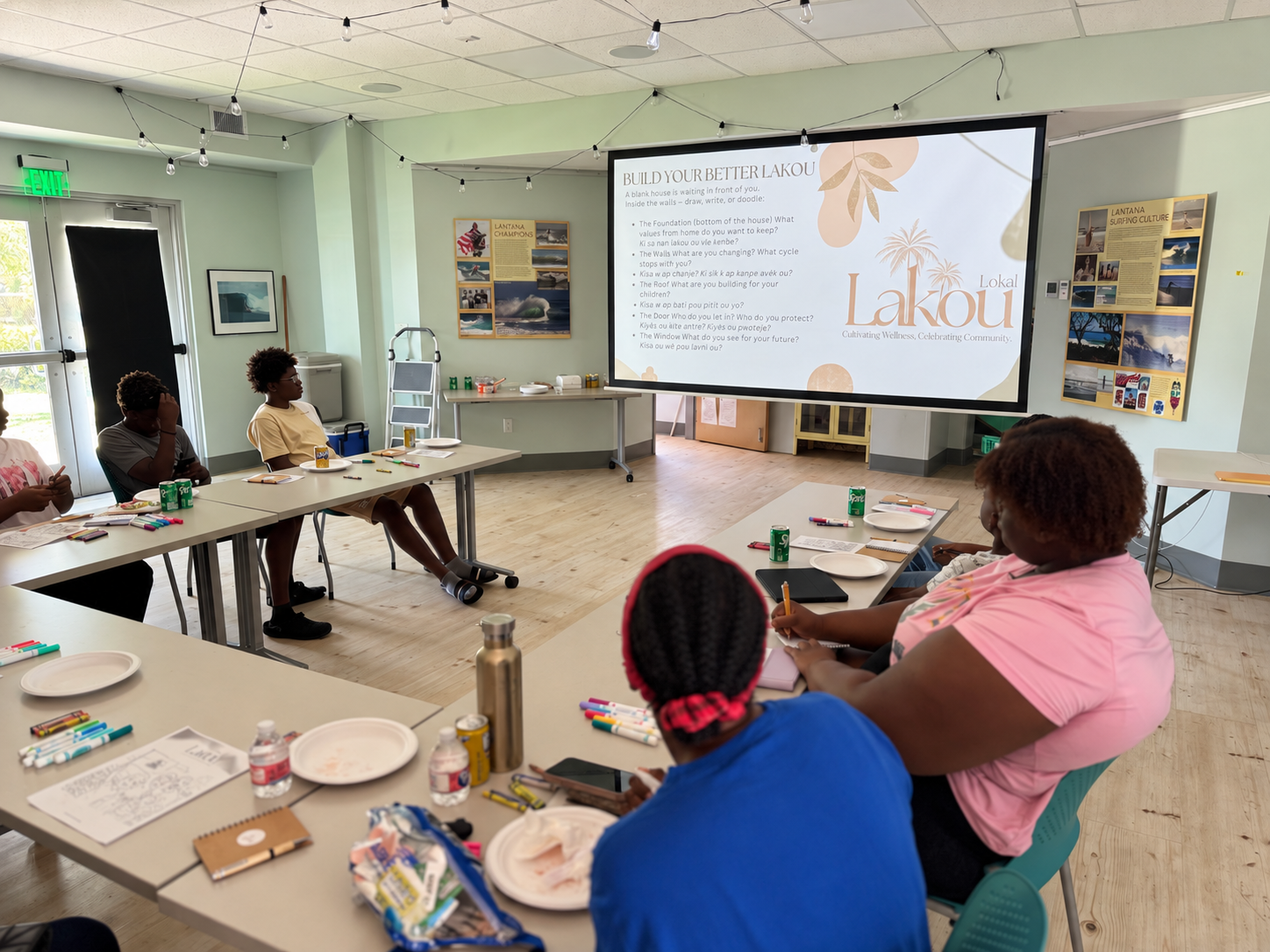 Youth and parents writing and drawing together at tables during a Lakou Lokal workshop